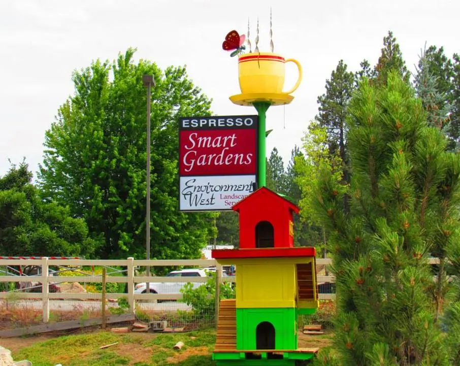 Colorful goat climbing house topped with a Smart Gardens sign and a large coffee cup