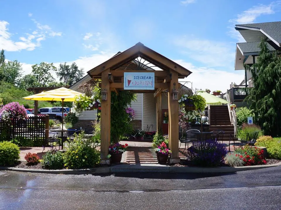Timber entrance arch surrounded by flower pots, with patio seating beyond