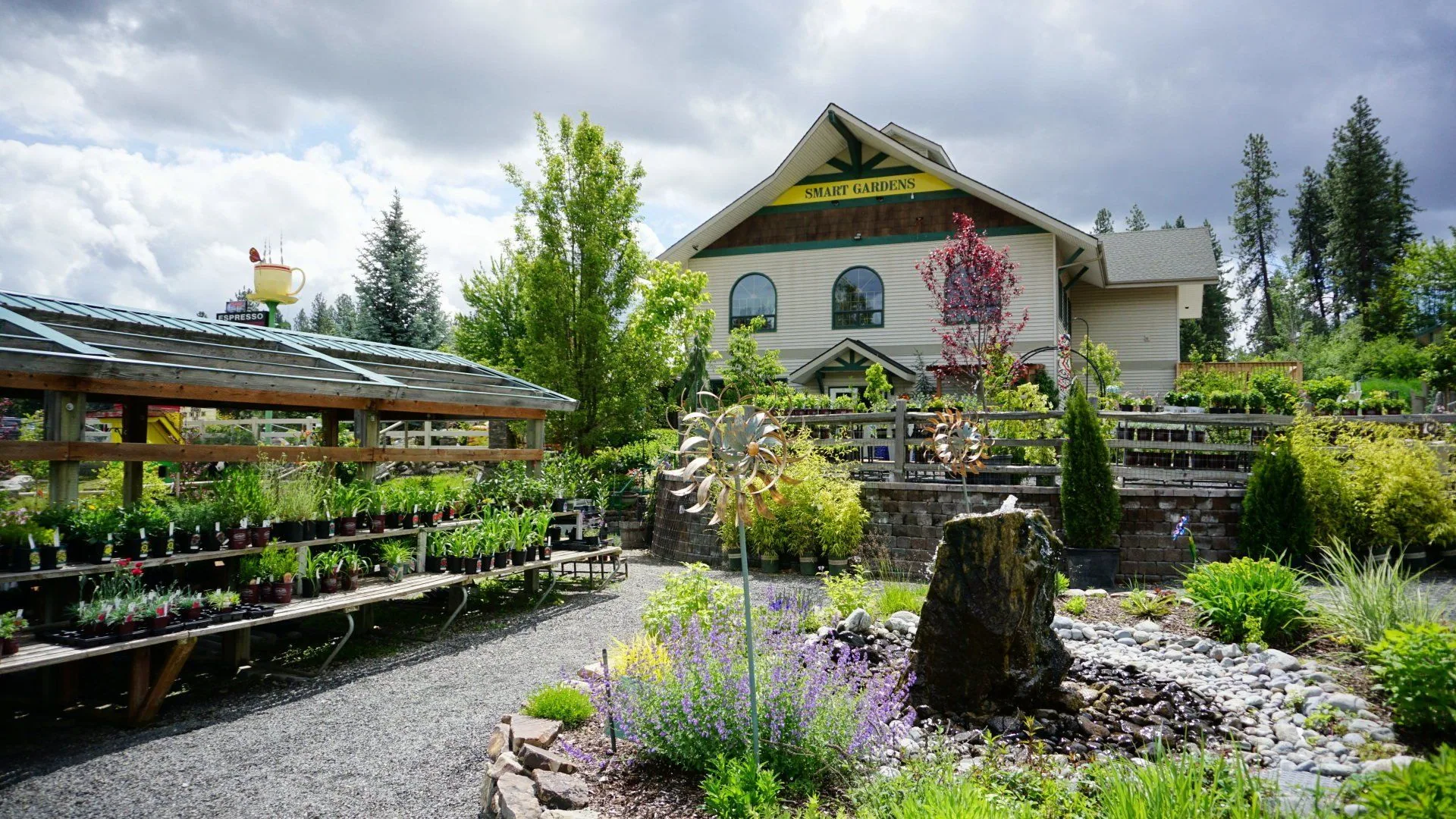 The Smart Gardens Nursery building behind gravel paths, lavender, a boulder fountain and shelves of plants